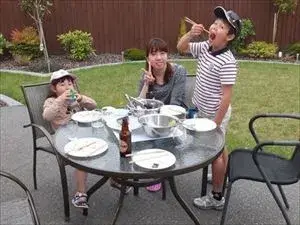 ホームステイゲストの方からの勇気が出るアドバイスはこちら ホームステイゲストと子どもたち2人がお庭のテーブルでディナーを楽しんでいる様子